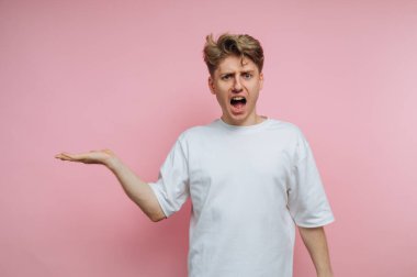 Pembe arka planda iddialı bir jestle bağırarak öfke ve hayal kırıklığını ifade eden genç bir adamın portresi.