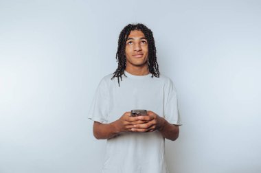 Genç adamın portresi, telefon ekranına bakarken düşünceli görünüyor. Konsantrasyonunu ve beyaz arka plana olan bağlılığını gösteriyor.