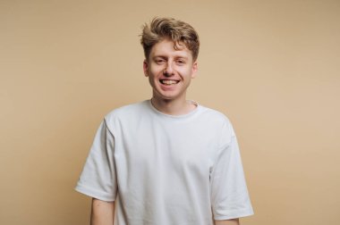 Neşeli genç adamın portresi gülümsüyor, bej arka planda sıcaklık ve dostluk yayıyor.