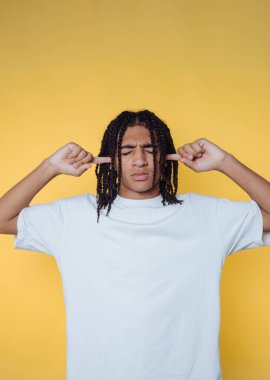 Örgülü saçlı genç adamın portresi, sarı arka planda barış ihtiyacını temsil eden kulaklarını kapatırken hayal kırıklığını gösteriyor.