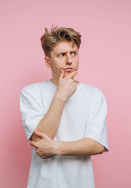 Düşünceli bir ifadeyle genç bir adamın portresi. Pembe arka planda dikilirken kafa yoruyor.
