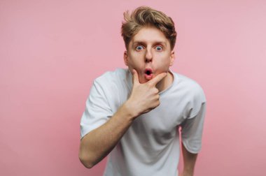 Genç, şaşırmış bir adamın portresi çenesini tutarken ağzını açar ve pembe arka planda bir sürpriz anı yakalar.