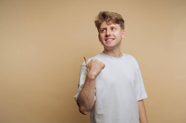 Genç ve enerjik bir adamın portresi gülümsüyor ve başparmak kaldırıyor, bej arka planda pozitiflik ve kendine güven gösteriyor