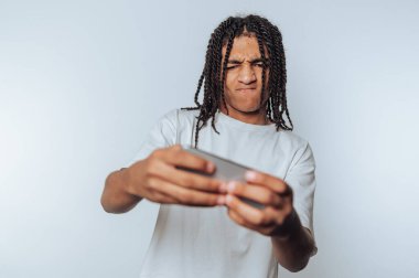 Genç bir adamın portresi, bir telefon kullanırken konsantrasyonunu bozuyor, nişanı gösteriyor ve beyaz arka plana odaklanıyor