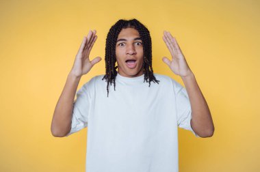 Genç adamın portresi, sarı arka planda ellerini kaldırarak şok edici bir ifade sergiliyor.