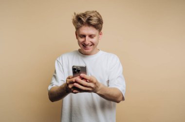 Akıllı telefonuyla meşgul olan genç adamın portresi, bej arka planda bir neşe ve bağlantı anı yakalıyor.