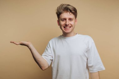 Genç memnun bir adamın portresi açık bir avuç içini dostça bir ifadeyle sunuyor, bej arka planda bir davet ya da fikir paylaşımı olduğunu gösteriyor