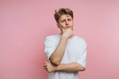 Düşünceli bir tavır sergileyen genç bir adamın portresi, pembe arka planda düşünceli bir şekilde poz verirken düşünceleri yansıtıyor.