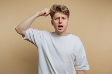 Genç adamın portresi, bej arka planda yakalanan bir durum üzerinde kafa karışıklığı ve hayal kırıklığını ifade eder.