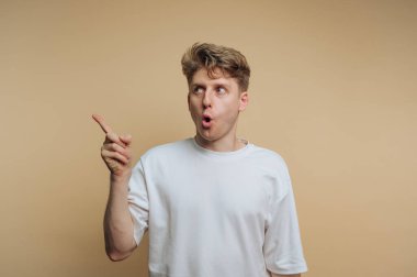 Genç adamın portresi şaşkınlıkla parmağını kaldırırken bej arka planda bir farkındalık ifadesi sergiliyor.