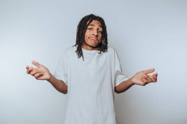 Omuzlarını silkeleyen genç bir adamın portresi, beyaz arka planda belirsizlik ve kararsızlığı ifade ediyor.