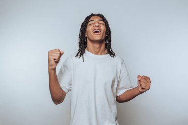 Neşeli yüzlü genç bir çocuğun portresi beyaz arka planda coşkulu ve kaygısız bir mutlulukla yumruklarını kaldırır.