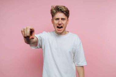 Yoğun bir ifadeyle genç bir adamın portresi kızgın bir şekilde izleyiciyi işaret ediyor, pembe arka planda güçlü duygular yakalıyor.