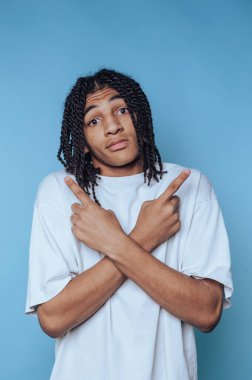 Örgülü saçlı genç adamın portresi, iki farklı yöne bakan, mavi arka plandaki kararsızlığı ve belirsizliği simgeleyen, karışık bir ifadeyle poz veriyor.