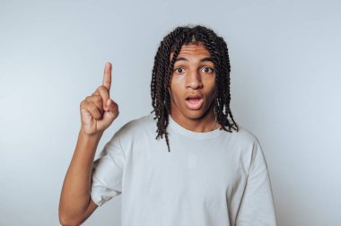 Örgülü genç bir çocuğun portresi şaşkınlık ve heyecanı ifade ediyor, beyaz arka planda bir parmağını neşeyle kaldırıyor.