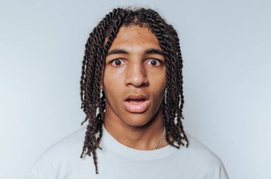 Genç bir adamın portresi, beyaz arka planda güçlü bir duygusal tepkiyi çağrıştıran geniş gözlü ve açık ağızlı hayret verici bir ifade sergiliyor.