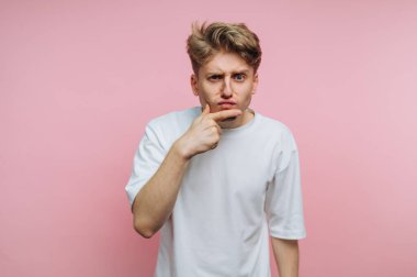 Genç bir adamın portresi, parmaklarını çenesine bastırırken düşünceli bir ifade sergiliyor. Pembe arka plan üzerine derin bir kafa karışıklığını sembolize ediyor.