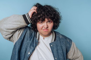 Kafası karışmış genç bir kadının portresi mavi arka planda kafa karıştırıcı bir bakış, harmanlayıcı bir mizah ve gündelik bir estetik ile kafalarını kaşır.