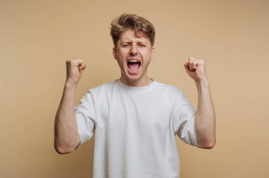 Genç bir adamın portresi neşe ve zafer saçıyor, zafer dolu bir anı bej arka planda yumruklarını kaldırarak gösteriyor.