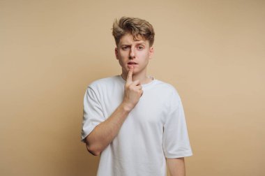 Genç adamın portresi, düşüncelere dalmış gibi yaparken parmağını ısırır. Bej arka planda bir anlık tefekkür ve içgözlem anı yakalar.