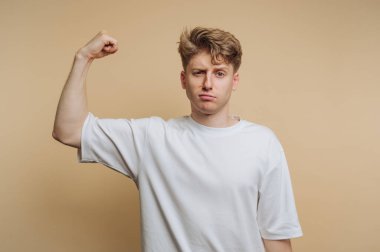 Genç adamın portresi, bej arka planda rahat bir tişört giyerken gücünü ve özgüvenini gösteriyor.