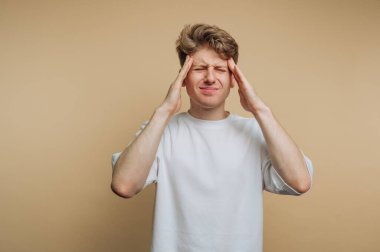 Sıkıntılı bir bakışla genç bir adamın portresi, kafasını endişe içinde tutmak, bej arka planda stres ya da hüsranı iletmek