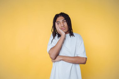 Saçları örgülü genç bir adamın portresi. Elini çenesini desteklemek için kullanıyor. Sarı arka planda düşünceli bir görünüm sergiliyor.