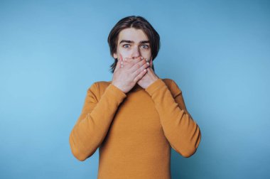 Turuncu boğazlı genç adamın portresi mavi arka planda elleri ile ağzını kapatıyor.