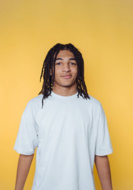 Uzun örgülü saçları olan neşeli bir gencin portresi sarı arka planda duruyor.