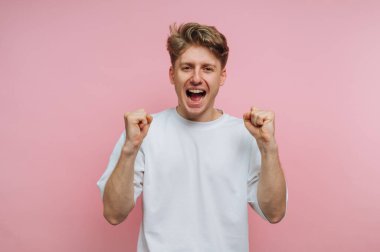 Neşeli genç adamın portresi yumruklarını kaldırarak kutluyor. Pembe arka planda heyecan ve zafer ifade ediyor.