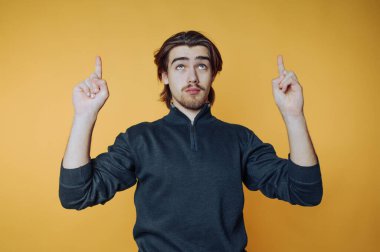 Siyah balıkçı yaka giyen genç adamın portresi yukarı doğru sarı arka planda derin derin bakıyor.