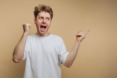 Genç adamın portresi enerjik bir şekilde bej arka planda bir kutlama ifadesiyle kenarı işaret ediyor.