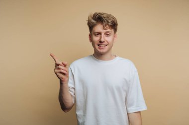 Genç ve neşeli bir adamın portresi bir ilham anını sembolize etmek için parmağını kaldırır, bej arka planda sıradan bir portrede yakalanır.