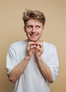 Bej arka planda elleri ile hareket ederken çekici, neşeli bir ifadeyle sırıtan genç bir adamın portresi