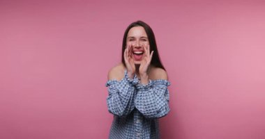 Gülücükler saçan genç bir kadının, güle güle dalgaları, pembe arka planda sıcaklık ve dostluk yaydığı görüntüler.