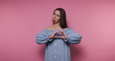 Elleriyle bir kalp şekli oluşturan genç bir kadın görüntüsü pembe arka planda sevgi ve sevgiyi simgeliyor.