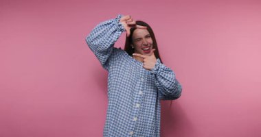 Genç ve neşeli bir kadının elleri pembe arka planda, yüzünü çerçeveleyerek poz verdiği görüntüler.