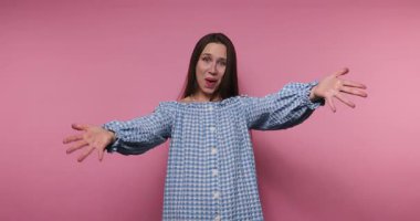 Genç, gülümseyen bir kadının pembe arka plandaki kollarını açtığı görüntüler.