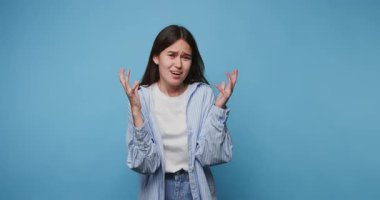 Genç bir kadının görüntülerinde hayal kırıklığına uğramış bir ifade var, elleri havada, mavi arka planda bir karışıklık var.