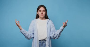 Genç bir kadının sakin ve meditasyonlu görüntüsü, sakin duruşuyla mavi arka planda gözleri kapalı bir şekilde görüntülenir.