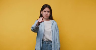 Genç bir kadının görüntüsü, sarı arka plana işaret ederken iddialı bir ifadeyle onaylamadığını gösteriyor.