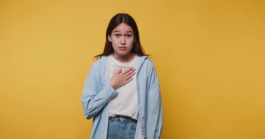 Düşünceli genç bir kadının elini göğsüne koyduğu görüntüler. Sarı arka planda samimiyet ve içtenlik gösteriyor.