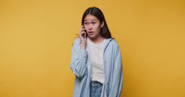 Telefonda endişeli görünen genç bir kadının görüntüsü, sarı arka planda duygusal durumunun altını çiziyor.