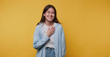 Genç, neşeli bir kadının, kameraya poz verirken gülüşü, sıcaklığını ve açıklığını sarı arka planda ışıl ışıl bir gülümsemeyle gösteriyor.