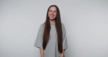 Rahatlamış gri gömlekli neşeli bir kadının saçlarıyla oynarken gülümsediği, açık arkaplanda neşeli bir kendini ifade etme anını yakaladığı görüntüler.