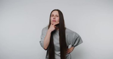 Gri gömlekli genç bir kadının görüntüsü düşünceli bir şekilde poz veriyor. Vücut dili, açık arkaplan üzerine kafa yoruyor.