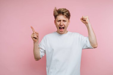 Bir adam heyecanla yumruklarını kaldırıp coşkuyla bağırarak sevinç ifade eder. Canlı pembe bir arka planın önünde duruyor, enerjisini sergiliyor..