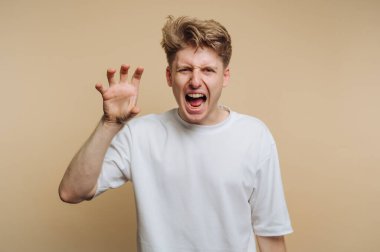 Genç bir adam yoğun duygular gösteriyor, bağırıyor ve elleriyle jestler yapıyor. Açık bej bir arkaplanda duruyor ve ifadesini vurguluyor..