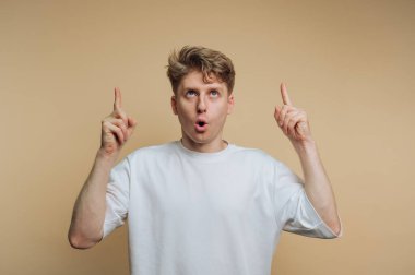 Ağzı açık duran bir insan, her iki parmağını da yukarı kaldırarak heyecanını gösterir. Tarafsız zemin, bireyin ifadelerini ve hareketlerini vurguluyor ve dinamik bir etki yaratıyor..