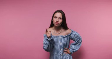 Genç düşünceli kadının görüntüsü, pembe arka planda şık bir kareli elbise giyerek yumruğunu kaldırıyor.